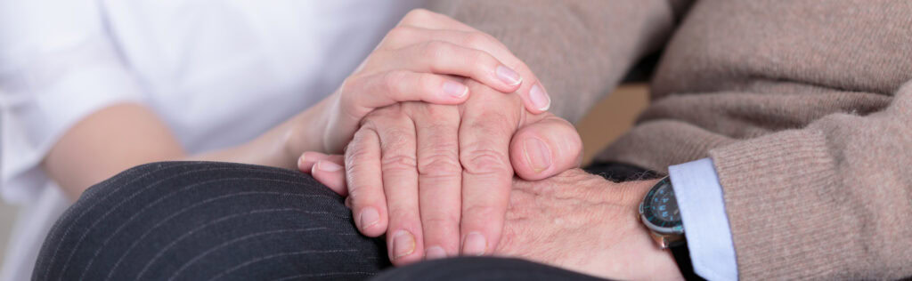 Family member holding the hand of a loved one receiving end of life care at home